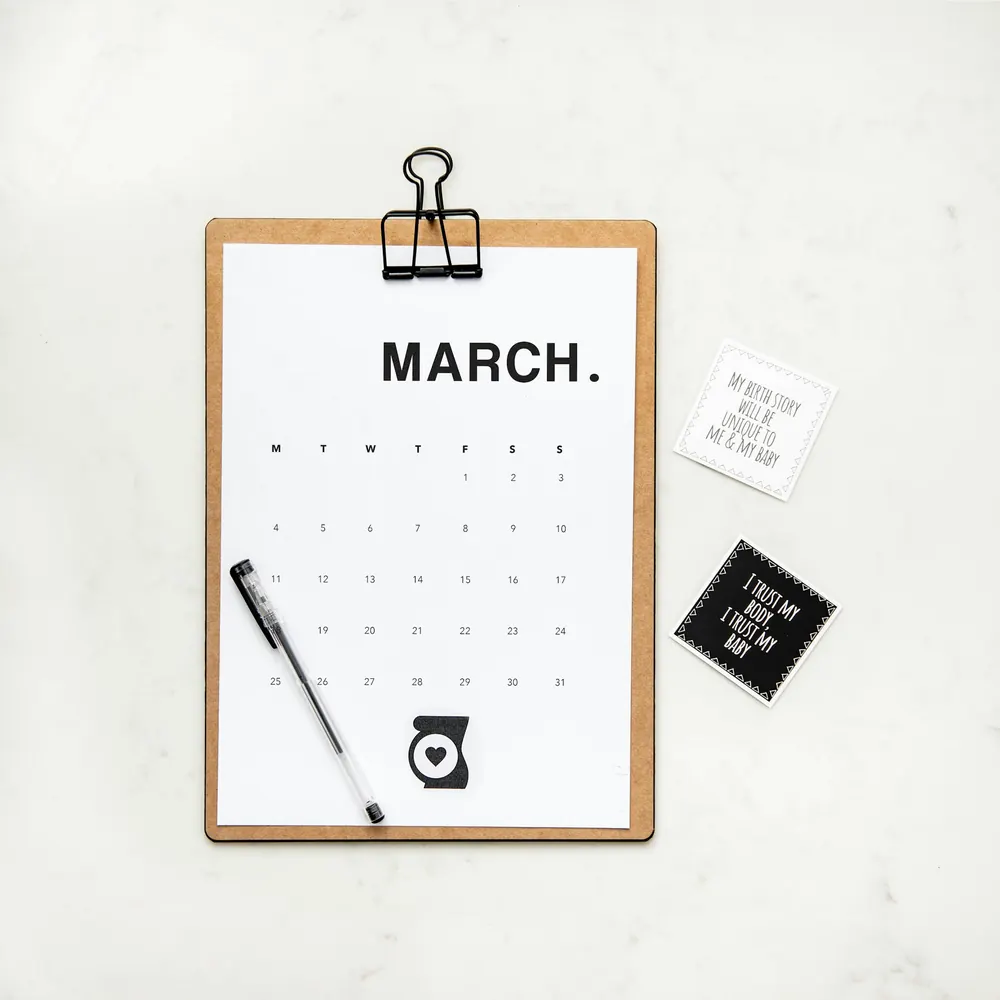 A monthly calendar for March clipped to a clipboard, with a pen beside it