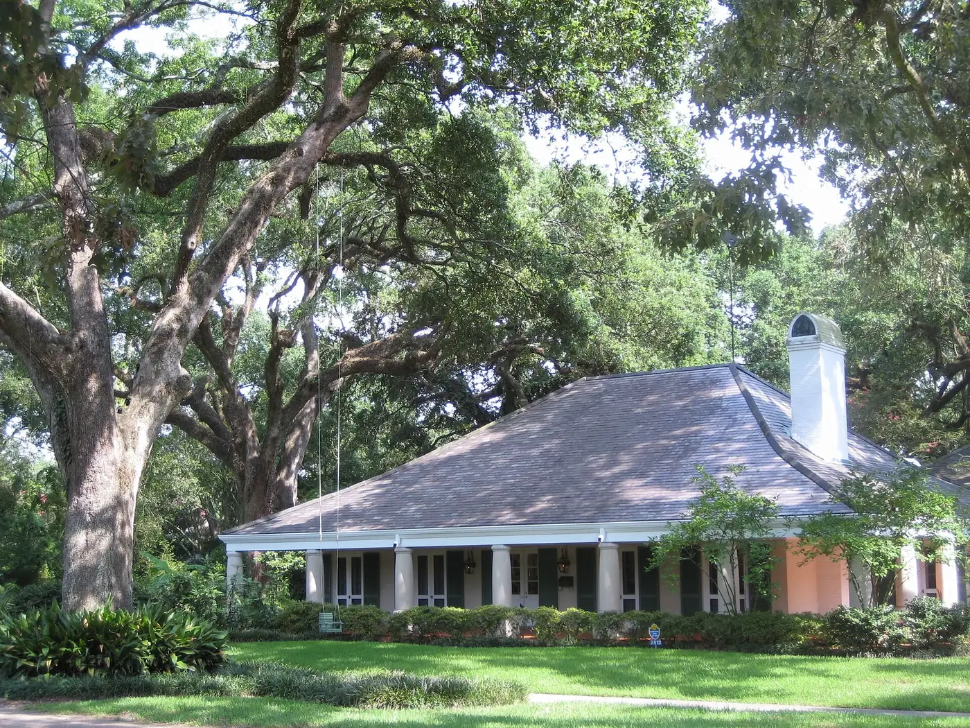 A Southern house with a deep front porch under large live oaks