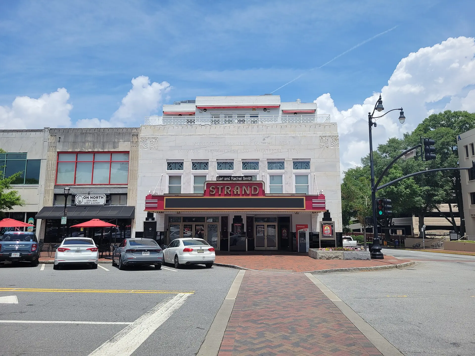 The white facade and red STRAND marquee of the Earl and Rachel Smith Strand Theatre on Marietta Square under a blue sky
